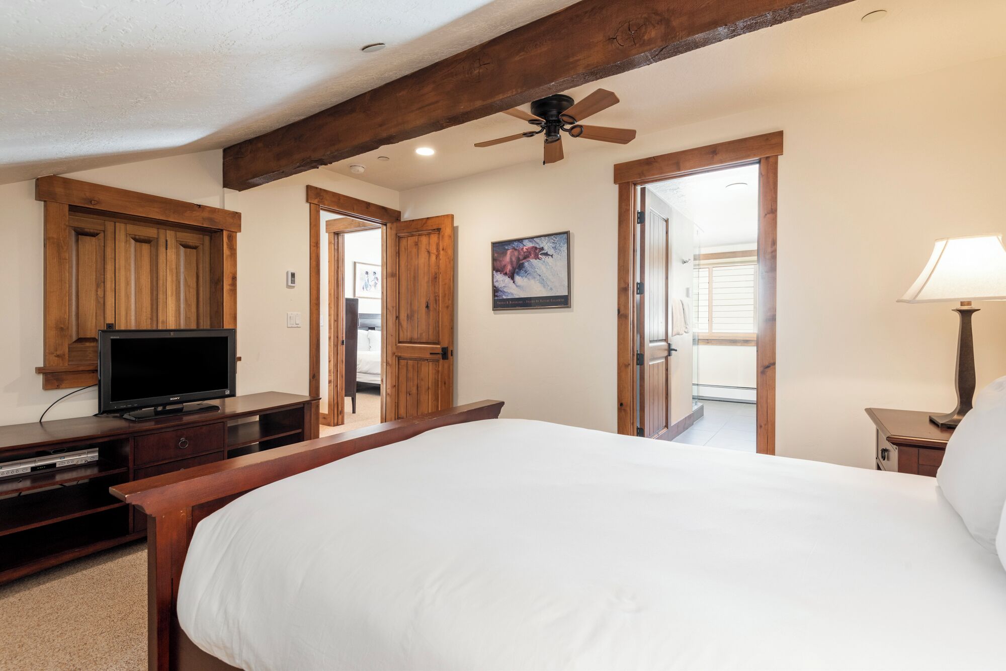 A bedroom with a large bed, wooden furniture, a television, and a ceiling fan.