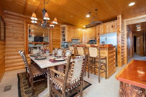 Interior de una cabaña de troncos con comedor, muebles de madera y cocina con electrodomésticos modernos.