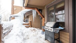 Una cabaña de madera con una parrilla afuera, nieve en el suelo y borbotones de hielo colgando del techo.