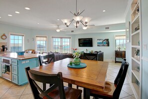 A spacious kitchen with a central island, dining area with chairs, and a TV mounted on the wall.