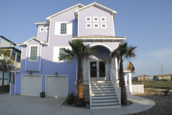 A two-story house with a front entrance, a garage, and a covered porch area with palm trees.