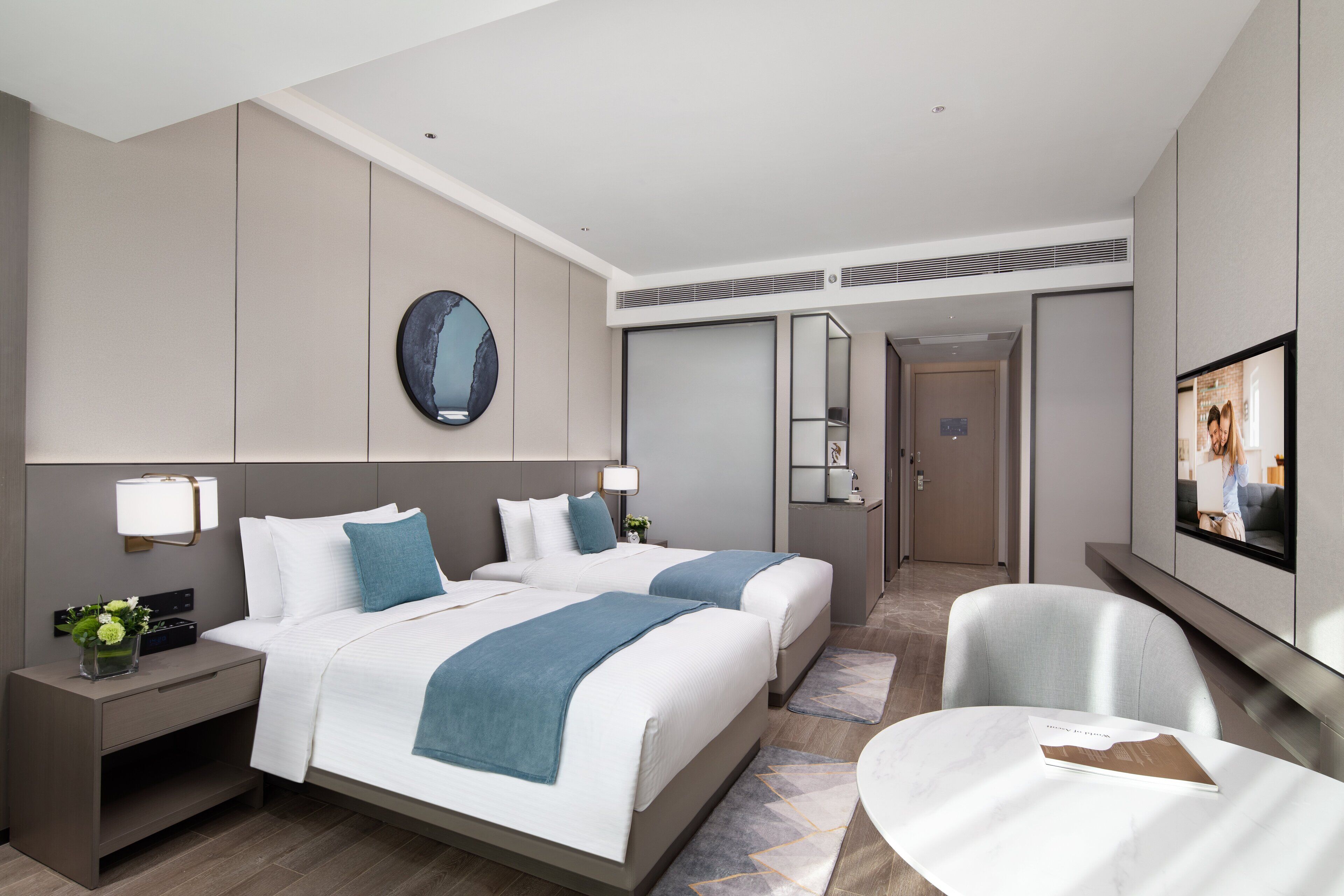 A modern hotel room with two beds, a seating area, and a TV.