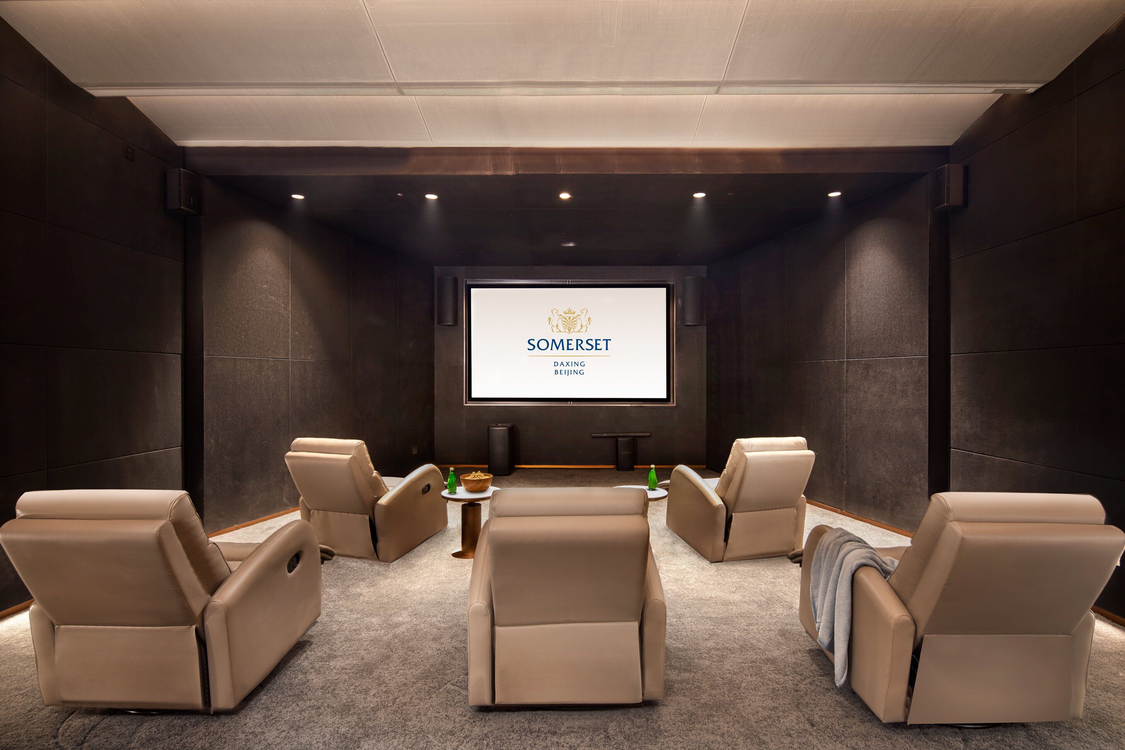 A modern cinema room with reclining seats, a large screen, and a dark, elegant interior.