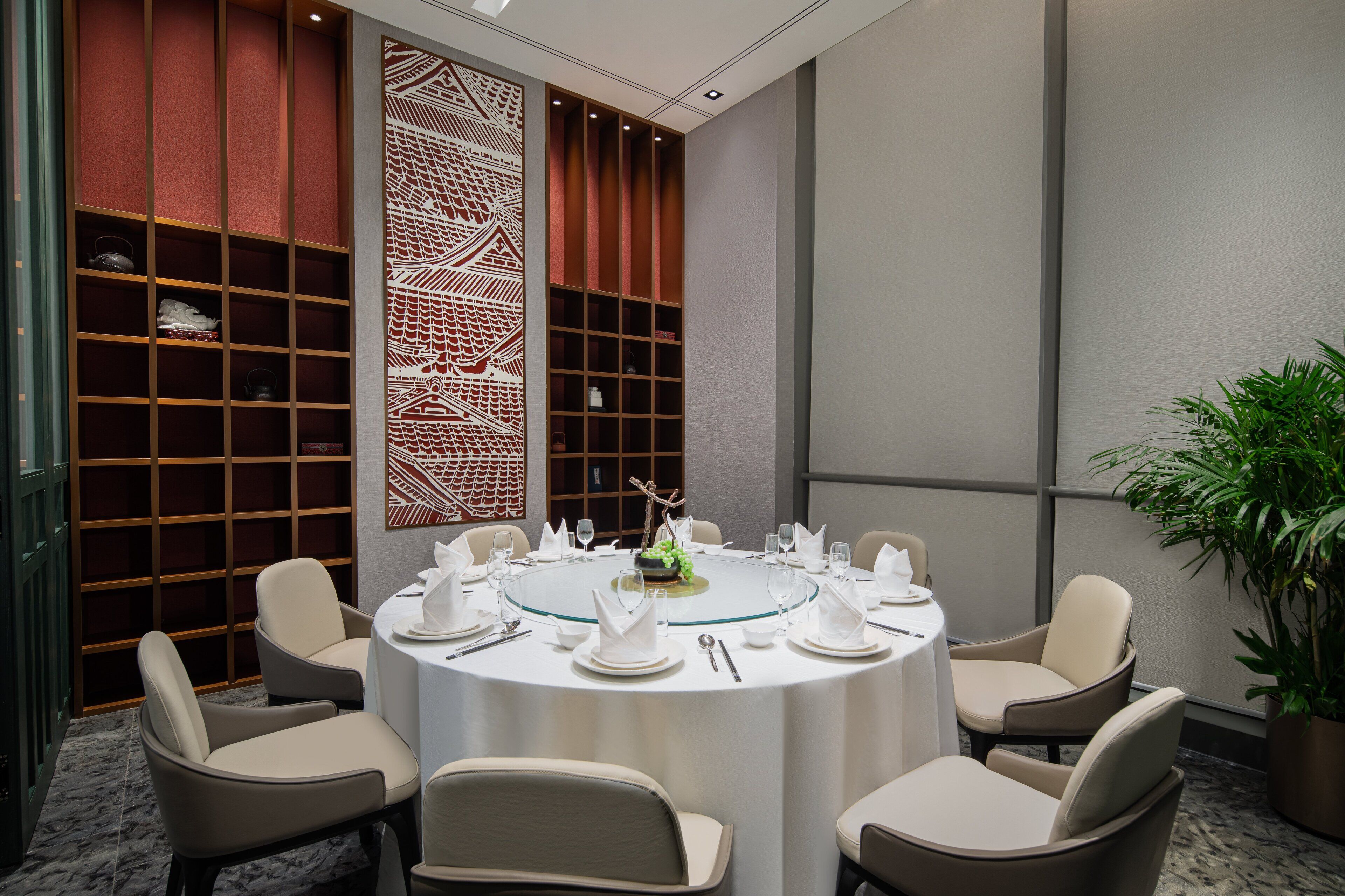 Una sala de conferencias con una mesa redonda dispuesta para seis personas, rodeada de sillas, con un panel decorativo y estanterías al fondo.
