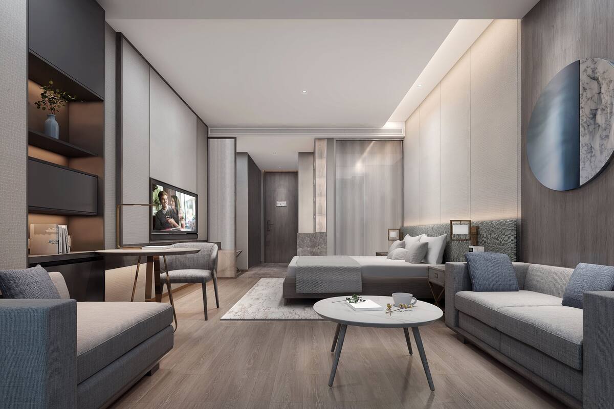 Quarto de hotel moderno com sofá, mesa redonda pequena, cama e televisão.