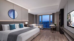 A modern hotel room with a large bed, a seating area, a TV, and a balcony with a city view. - Somerset Daxing Beijing (Daxing)