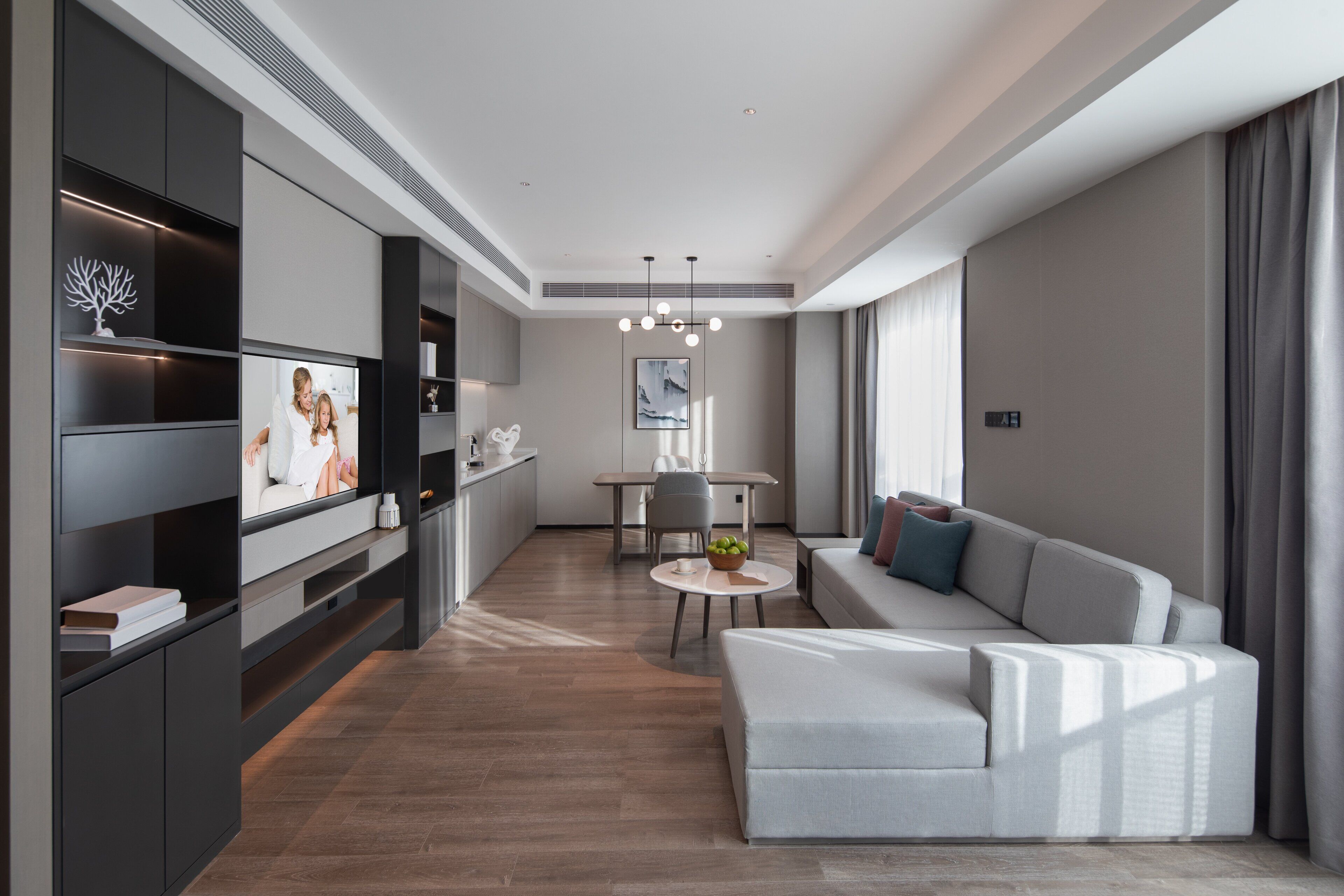 Una sala de estar moderna con un sofá gris, una mesa de centro y un televisor sobre un mueble negro.