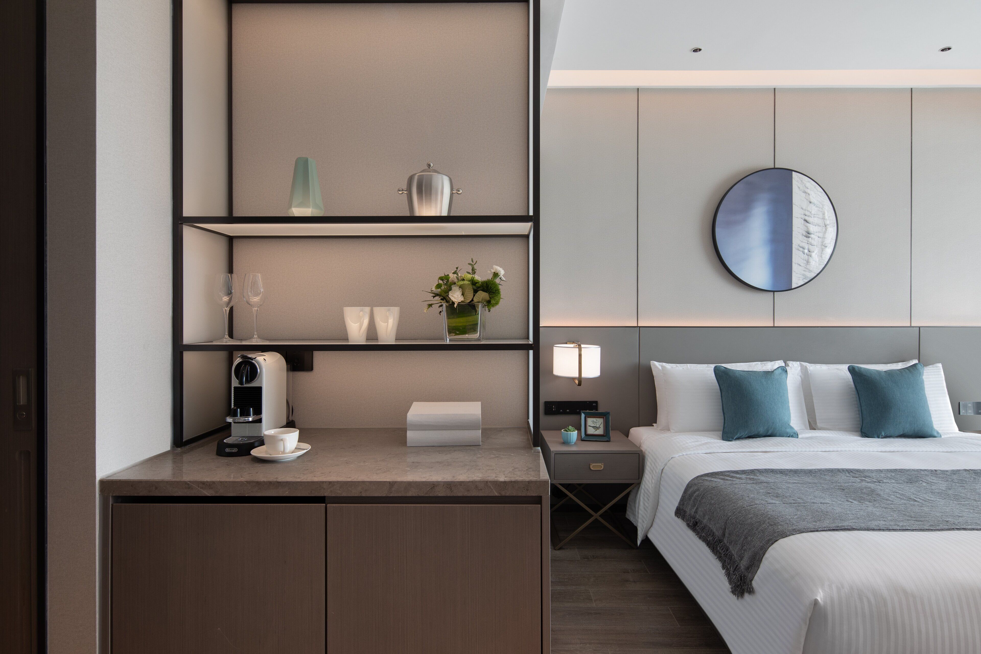 A hotel room with a bed, bedside table, lamp, and a coffee machine.