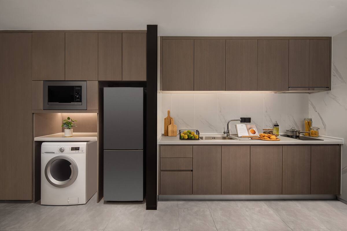 Uma cozinha moderna com máquina de lavar e secar integradas, micro-ondas, frigorífico e painel de parede em mármore.