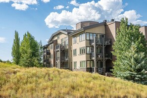 A multi-story building with balconies, surrounded by trees and grass.