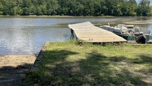 Une jetée en bois s’étendant sur un lac paisible, entourée d’une végétation luxuriante et bordée, au loin, par une forêt dense.