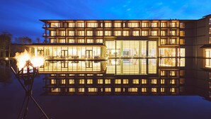Un hotel moderno con varios pisos y balcones, con una piscina reflectante al frente.