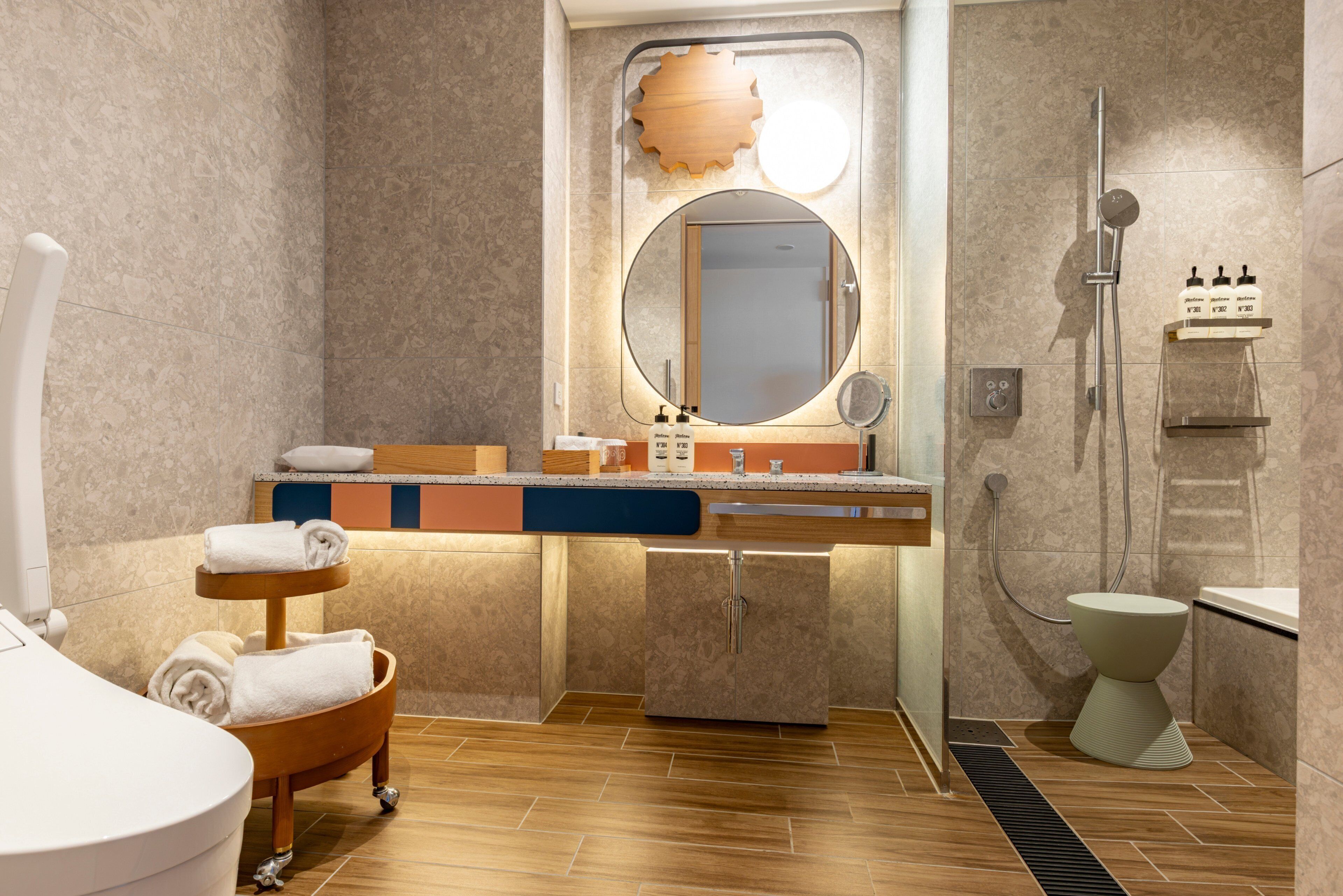 Une salle de bain moderne équipée d’un lavabo, d’un miroir, d’une douche, de toilettes et d’un porte-serviettes en bois.