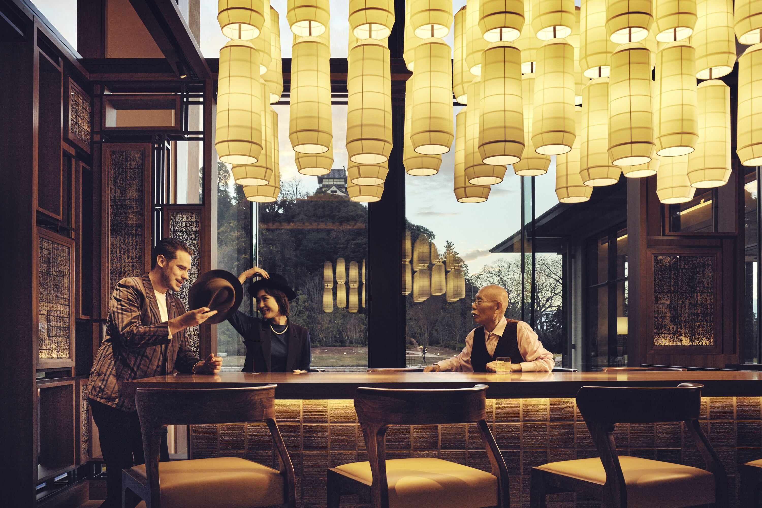 A restaurant with a long table, multiple chairs, and hanging lanterns.