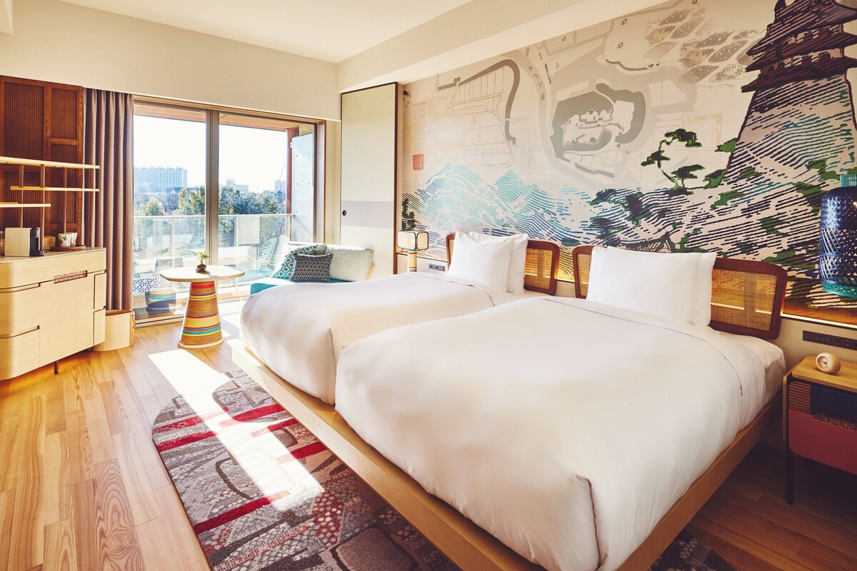 A modern hotel room with a large bed, a balcony, and a city view.