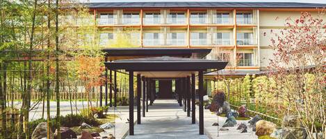 A covered walkway leading to a multi-story building with a modern design, surrounded by landscaped gardens and rocks.