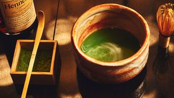 A wooden box with green powder, a ceramic bowl with green liquid, and a whisk on a wooden surface.