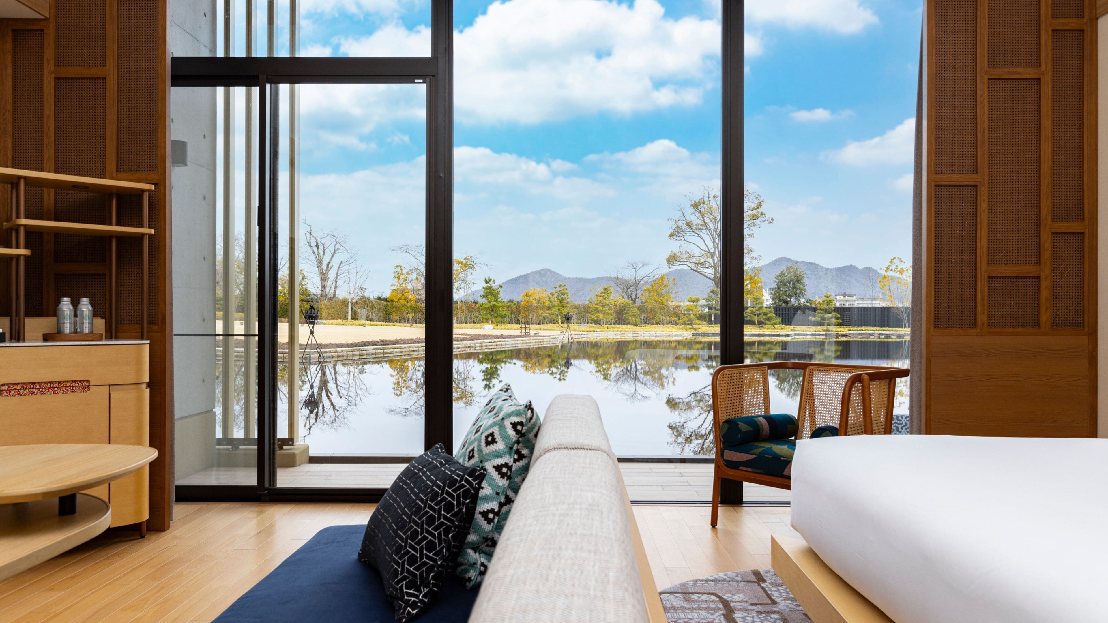 A modern room with a large window, a sofa, a bed, and a view of a lake and mountains.