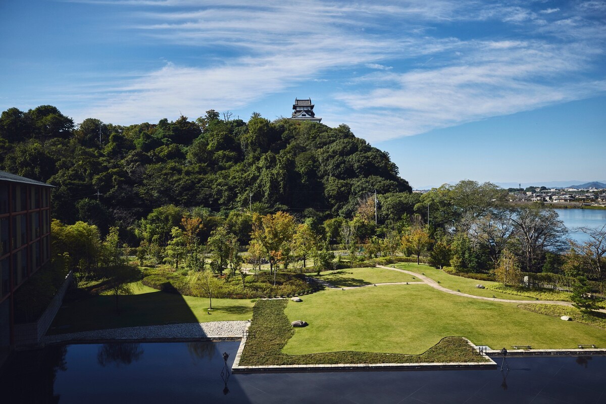 A traditional Japanese-style building on a hill with a view of a lake and a park below.