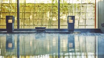A serene indoor pool area with a bench and two wall-mounted lights, surrounded by a bamboo fence and large windows.