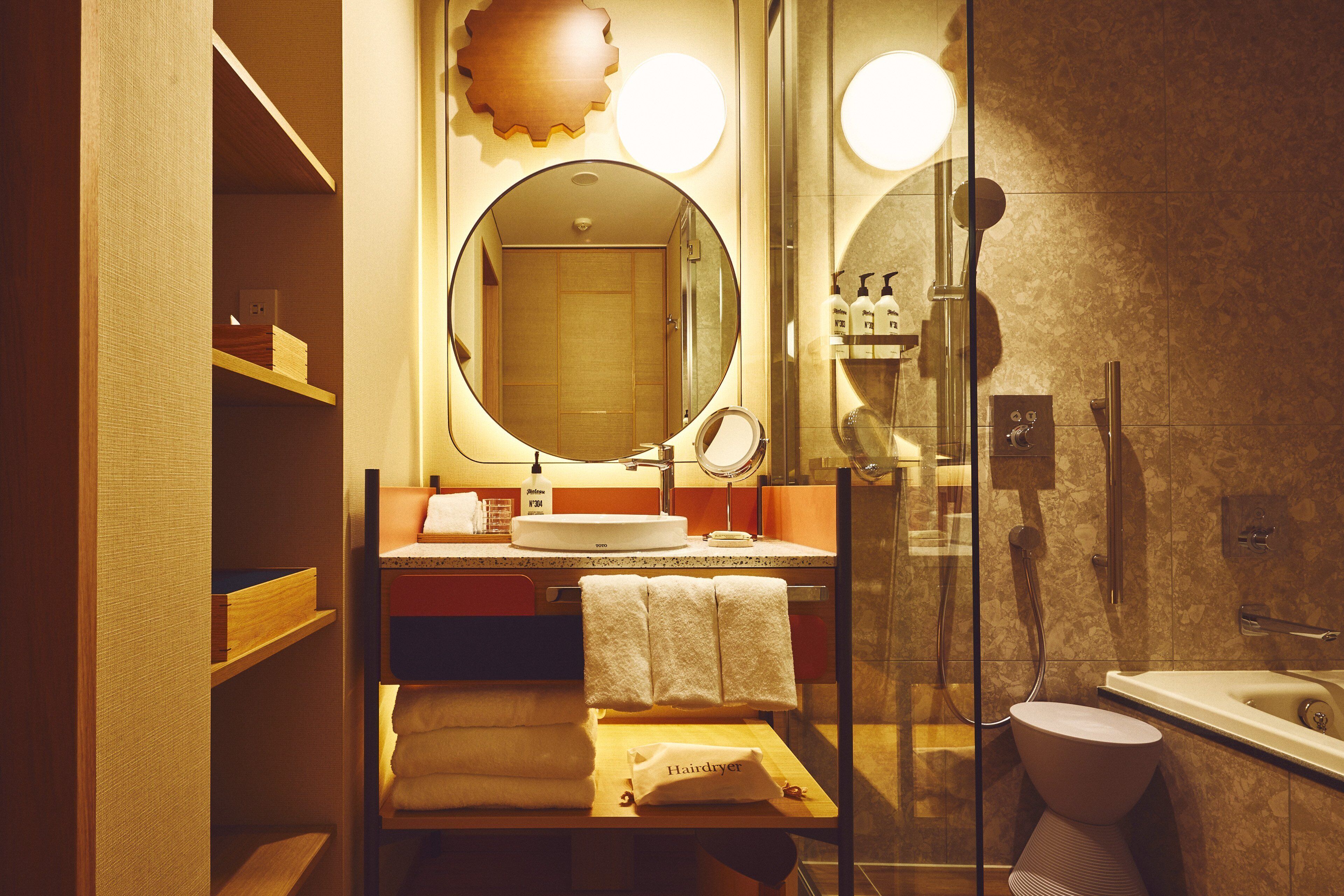 A modern bathroom with a glass shower enclosure, a round mirror, and a sink with a towel rack.