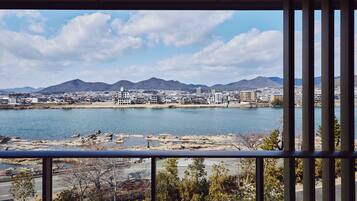 A cityscape with a large body of water, mountains in the background, and a view through a window with vertical blinds.