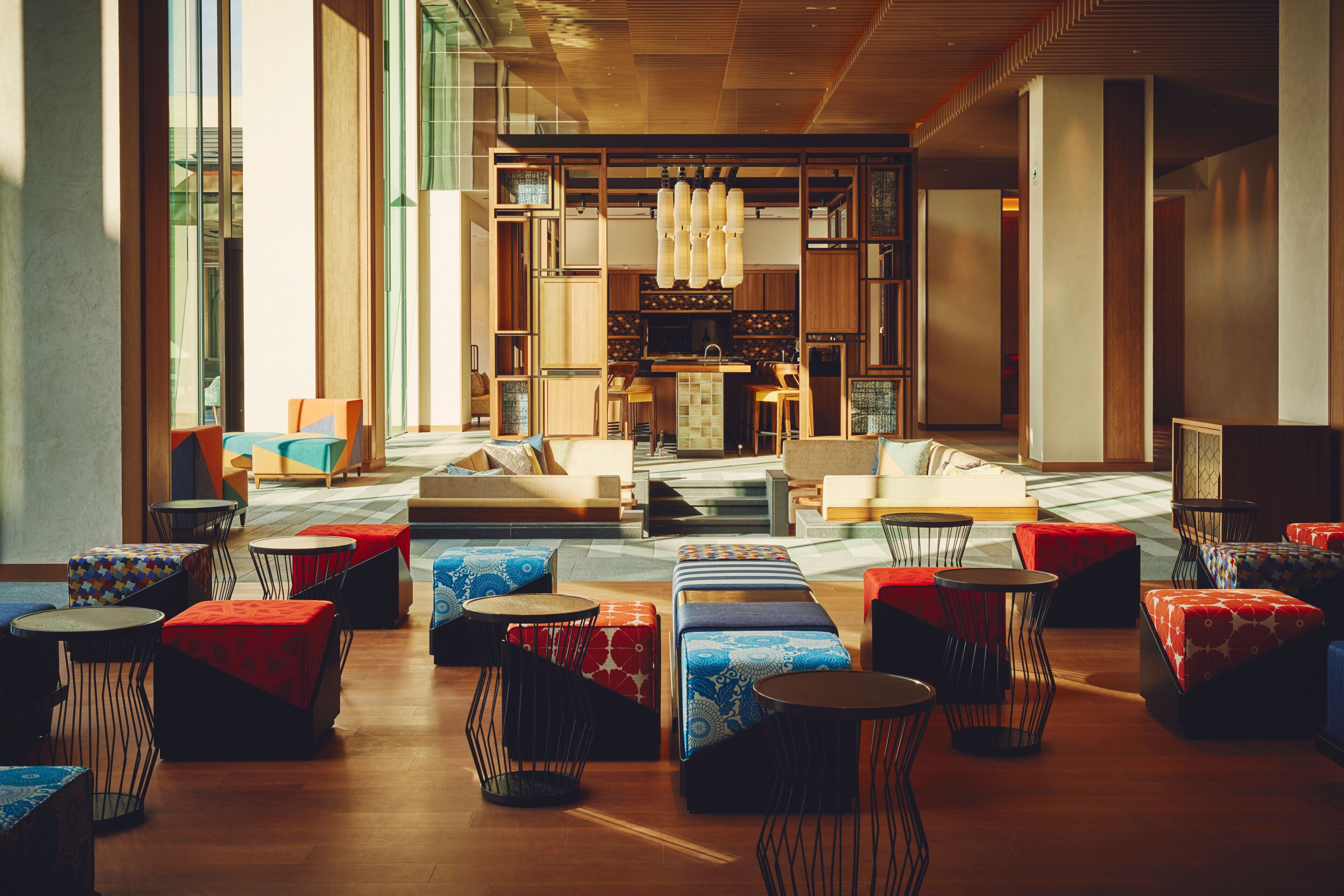 A modern hotel lobby with a central seating area, a bar, and large windows.