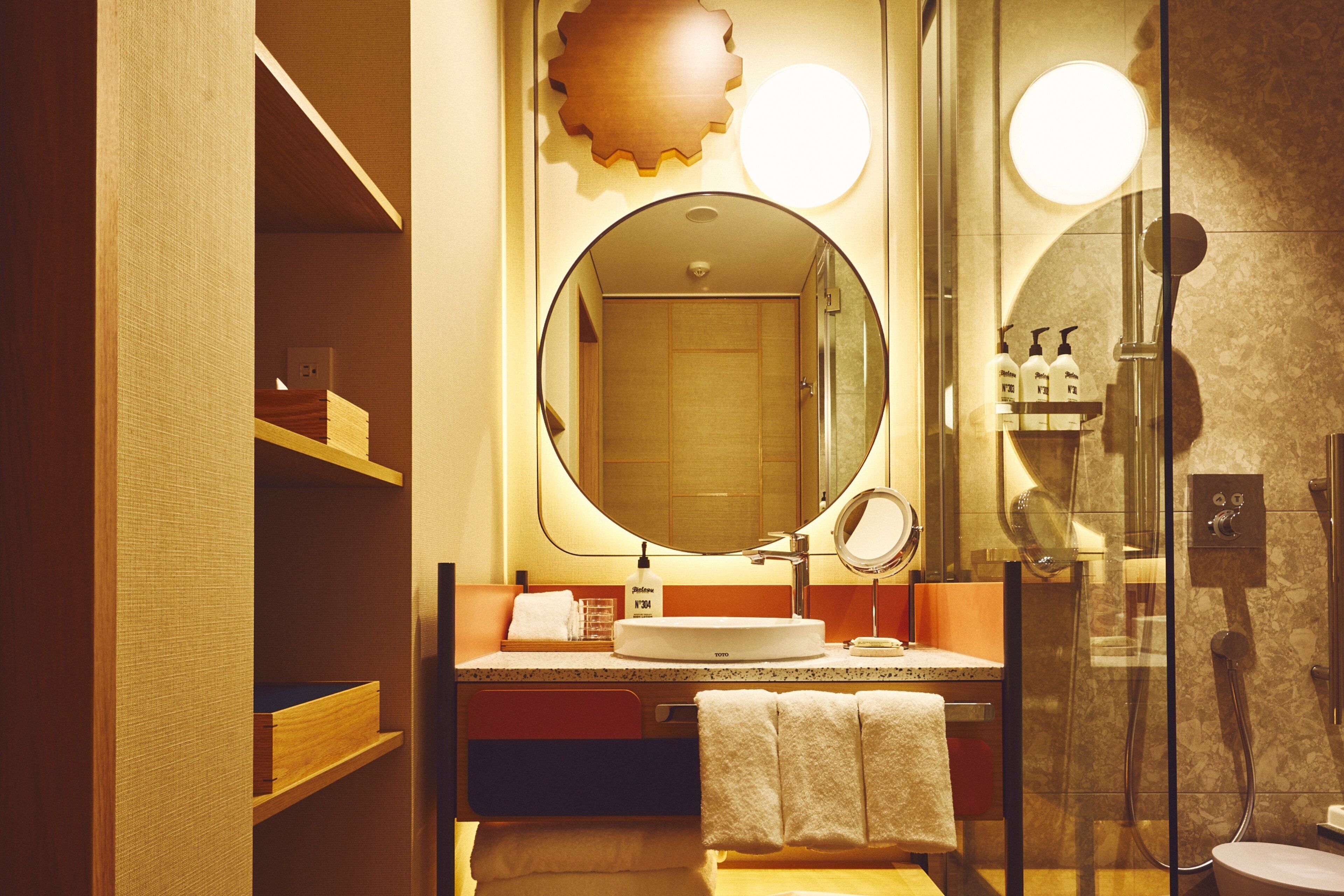 A modern bathroom with a round mirror, a sink, and a glass shower enclosure.
