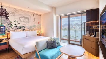 Une chambre d’hôtel moderne dotée d’un grand lit, d’un canapé, d’une table à manger et offrant une vue sur la ville et les montagnes grâce à de grandes fenêtres.