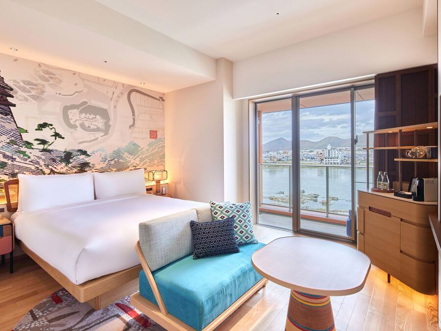 Une chambre d’hôtel moderne dotée d’un grand lit, d’un canapé, d’une table à manger et offrant une vue sur la ville et les montagnes grâce à de grandes fenêtres.