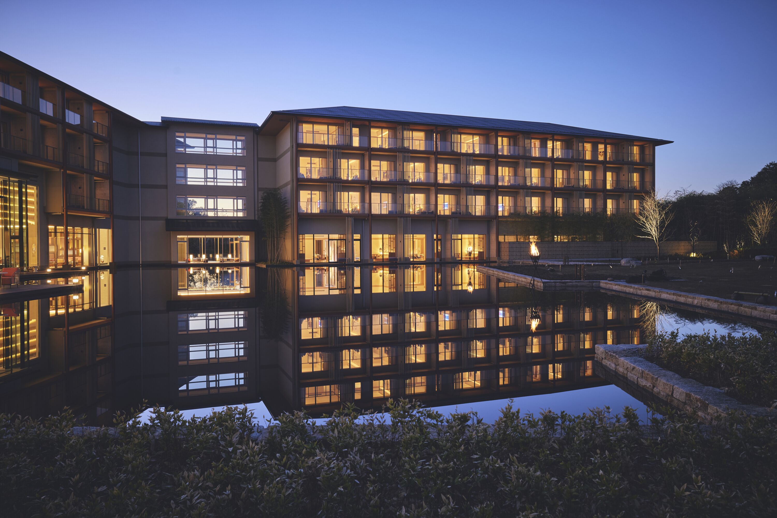 A modern building with multiple balconies and large windows, reflecting in a water feature in front.