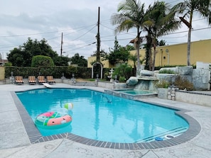Une piscine à bord incurvé, entourée de chaises longues et agrémentée d’une cascade artificielle en roches.