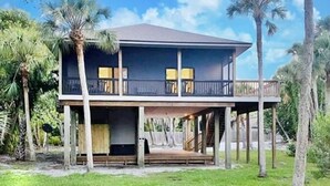 A two-story house with a balcony, surrounded by palm trees and a grassy lawn. - My Sea Shack~ 1 minute to beach, SH Club access, golf cart (Lee County)