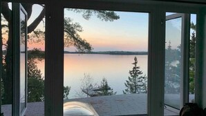 Et værelse med et stort vindue med udsigt til en rolig sø i solnedgangen.