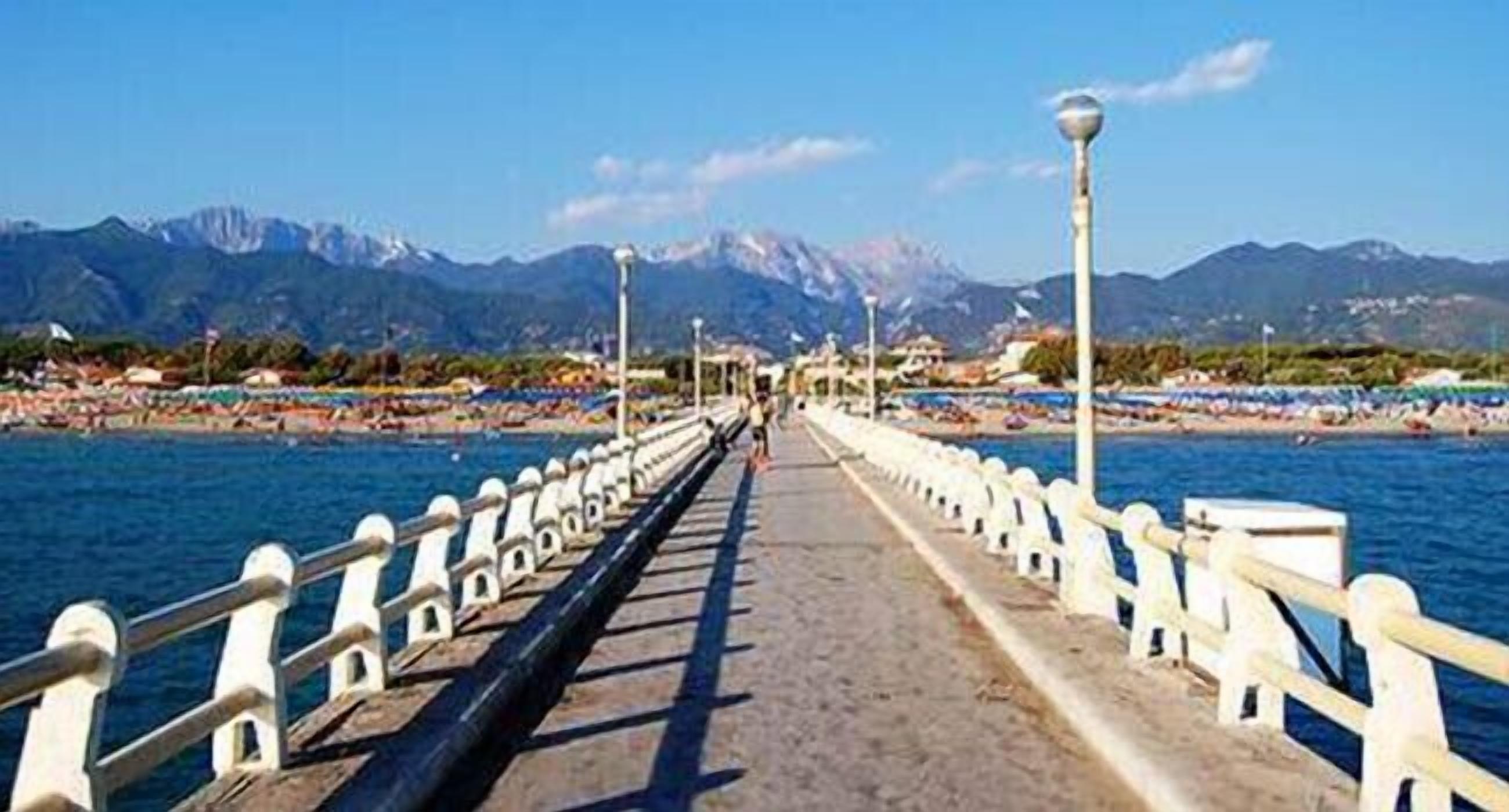A pier leading to a beach with mountains in the background.
