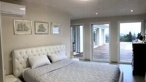 Une chambre dotée d’un grand lit, d’un ventilateur de plafond et offrant une vue sur l’extérieur grâce à une porte-fenêtre coulissante.