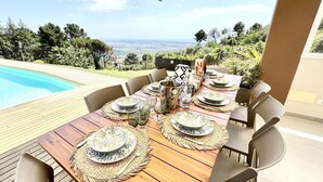 Une table dressée pour six personnes, avec assiettes, verres et une bouteille, donnant sur une piscine et un paysage pittoresque.