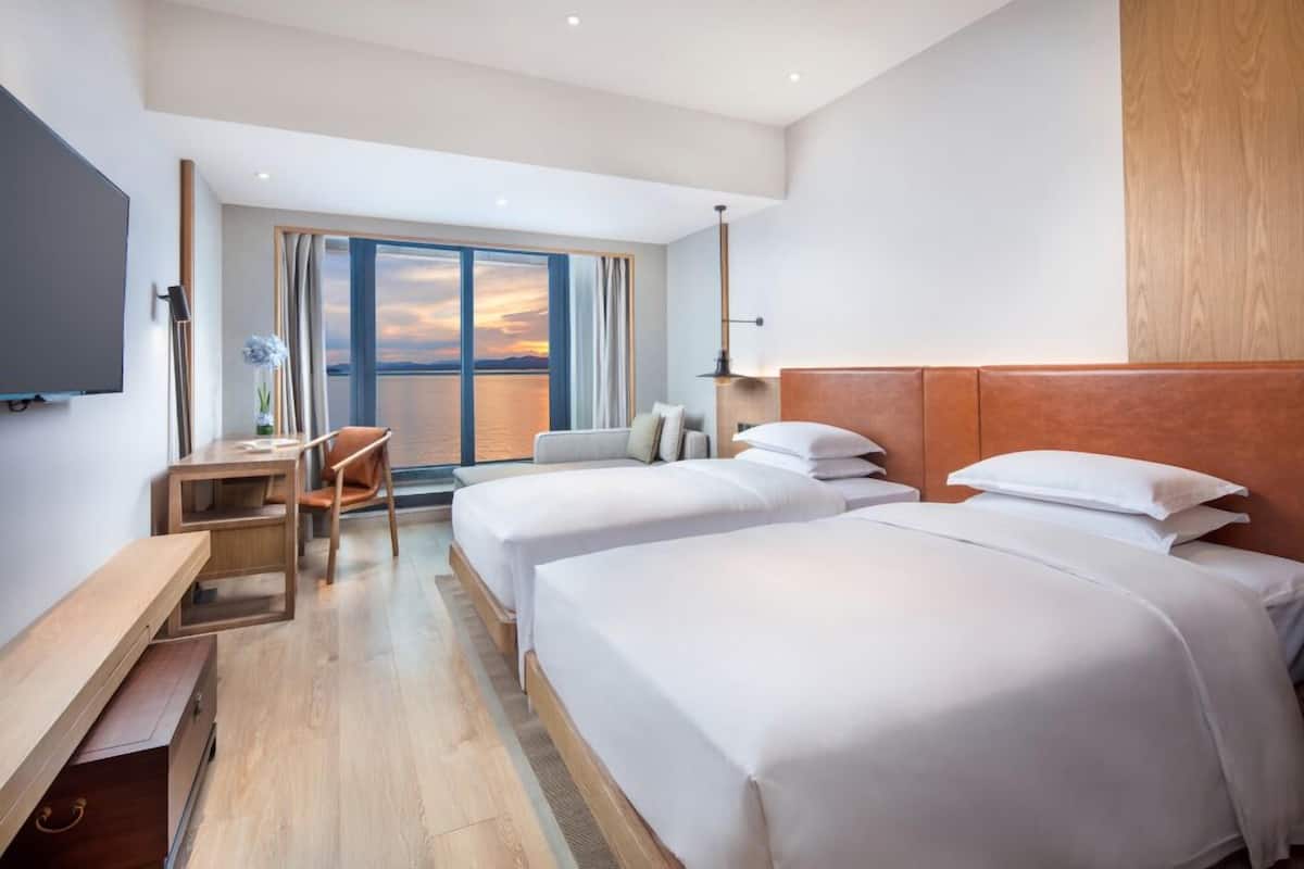 A hotel room with two beds, a desk, a chair, and a TV.