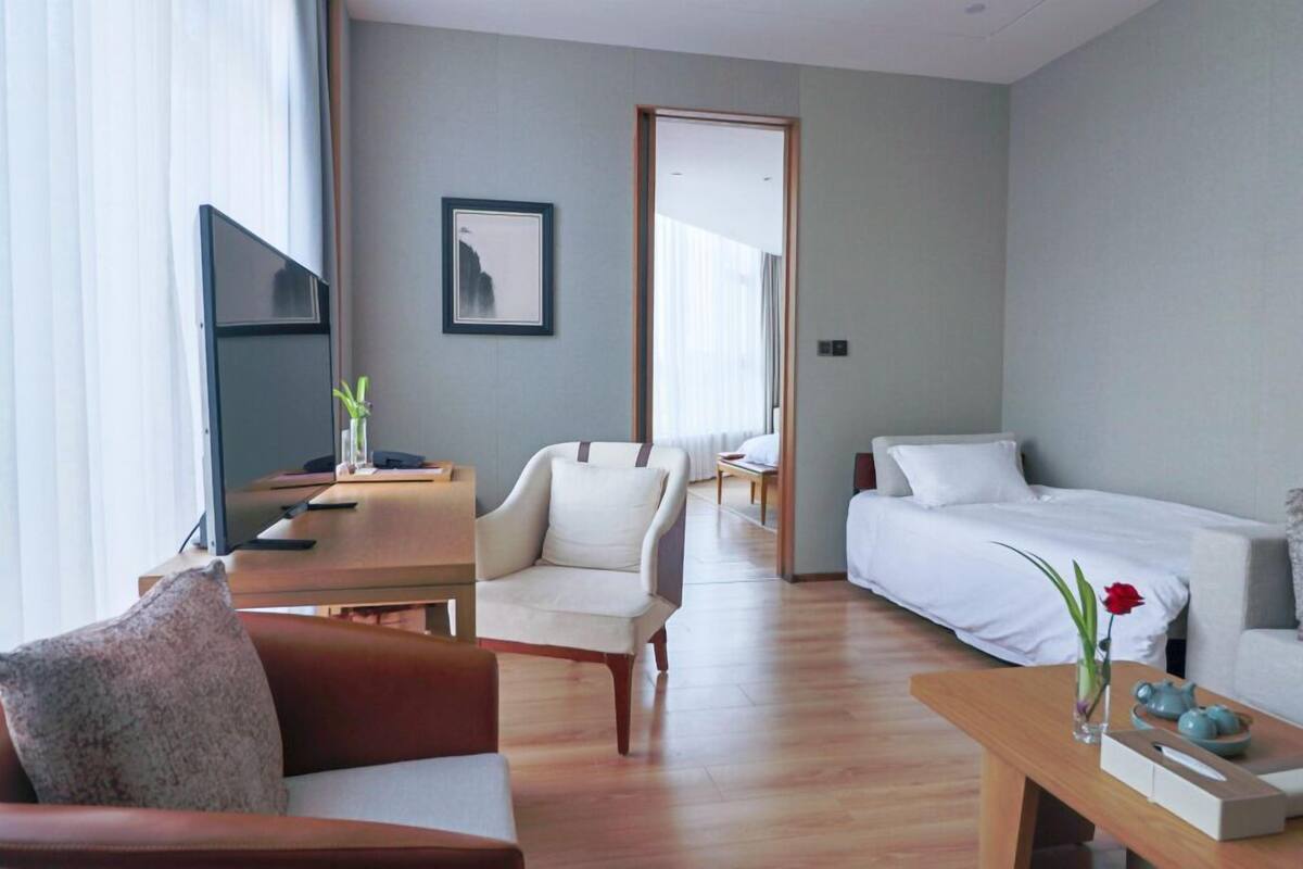 A modern hotel room with a wooden floor, a sofa, a bed, a desk, and a TV.