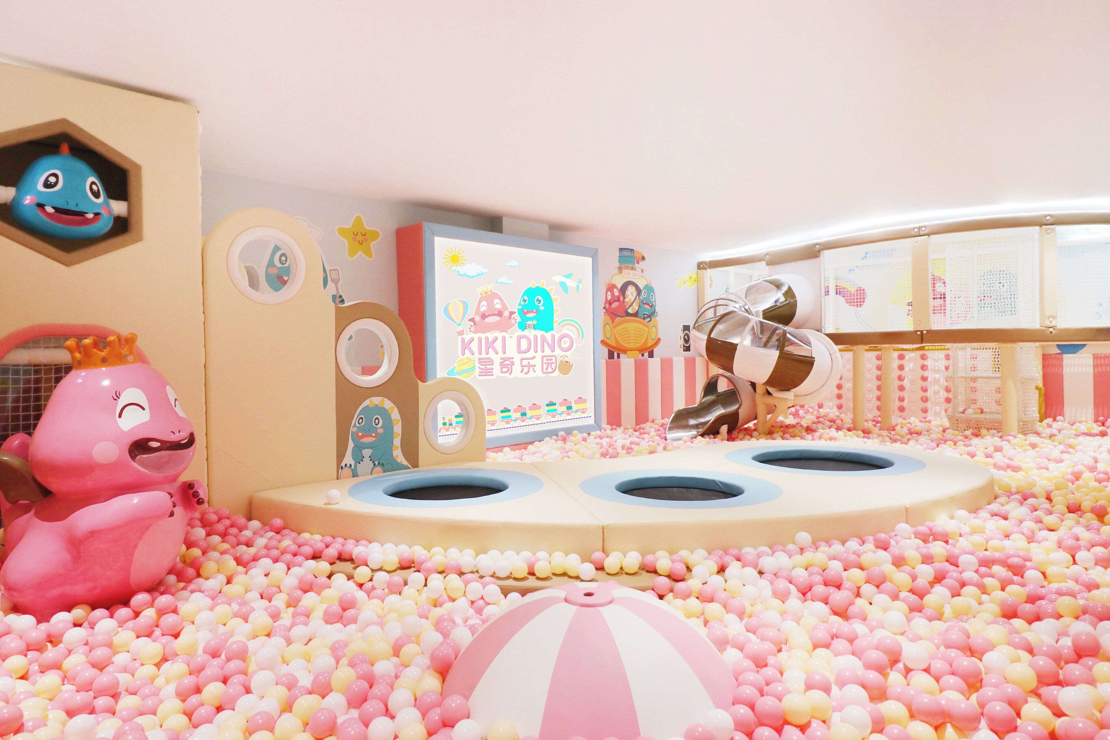 Un área de juegos infantiles con piscina de pelotas, juguetes inflables y un mural colorido.