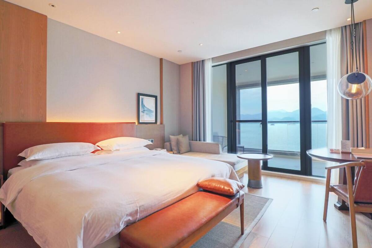 A hotel room with a large bed, a seating area with a table, and a view of the outdoors.