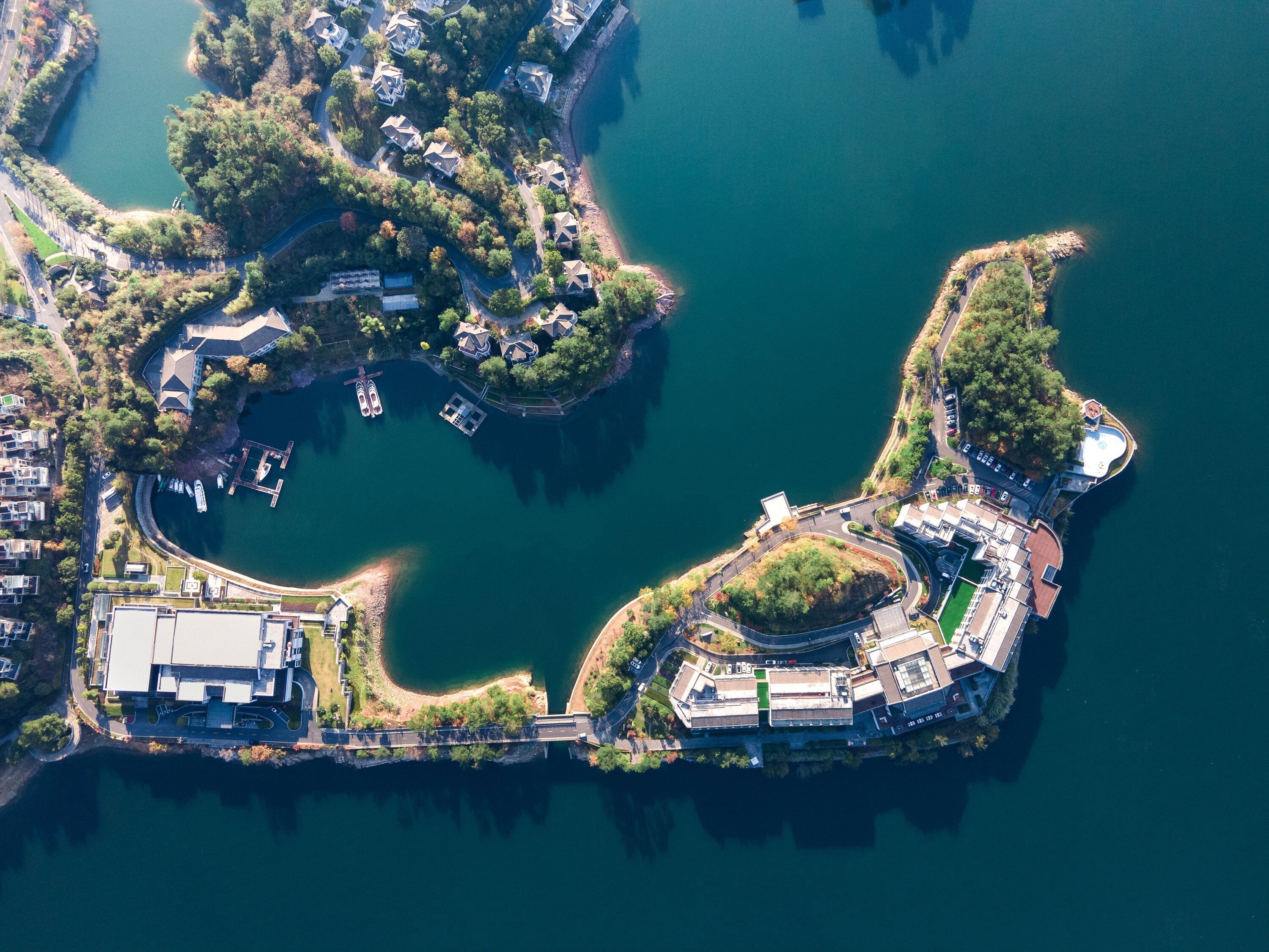 An aerial view of a lakeside property with a central building, surrounding roads, and docked boats.