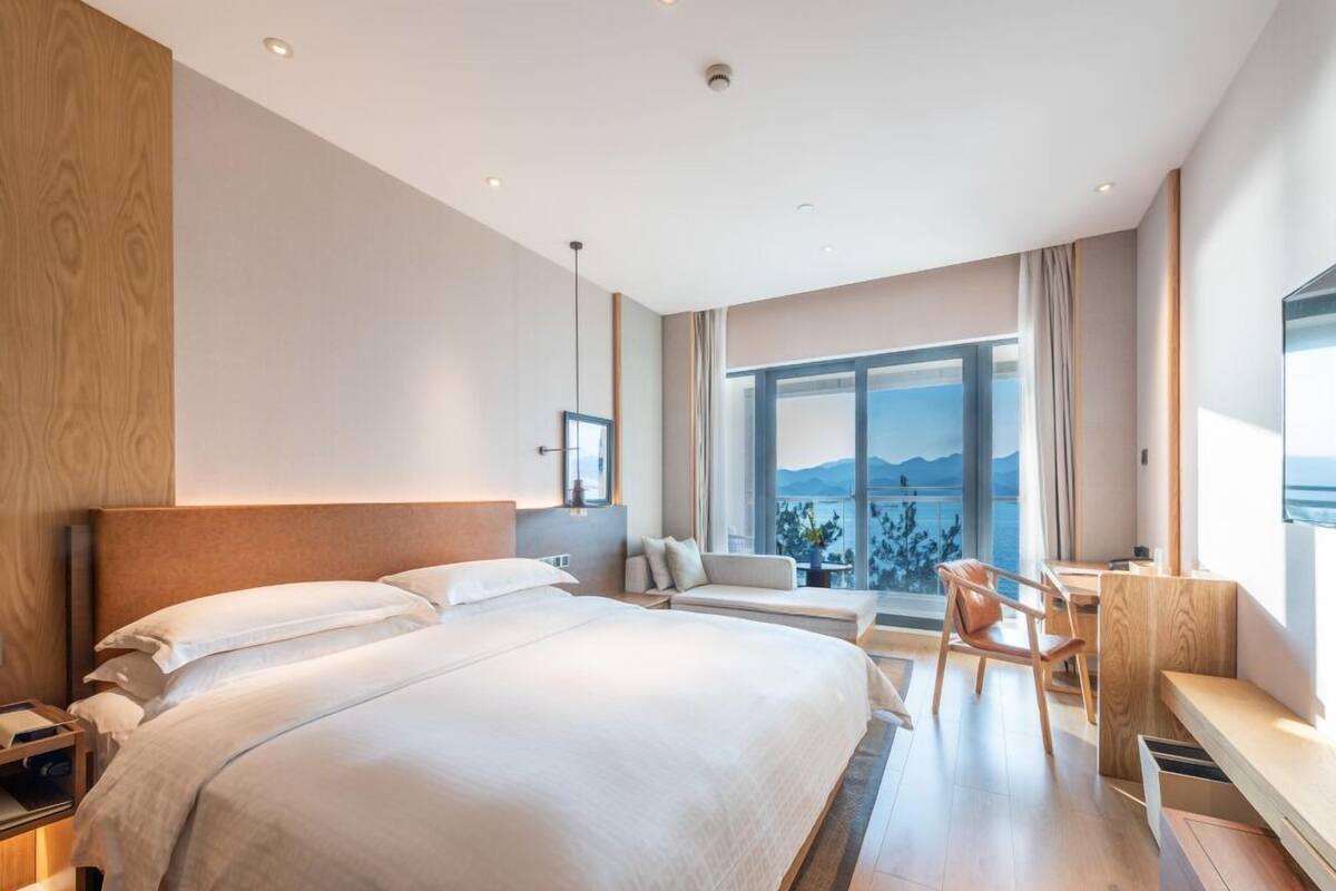 A modern hotel room with a large bed, a desk, and a view of the outdoors.