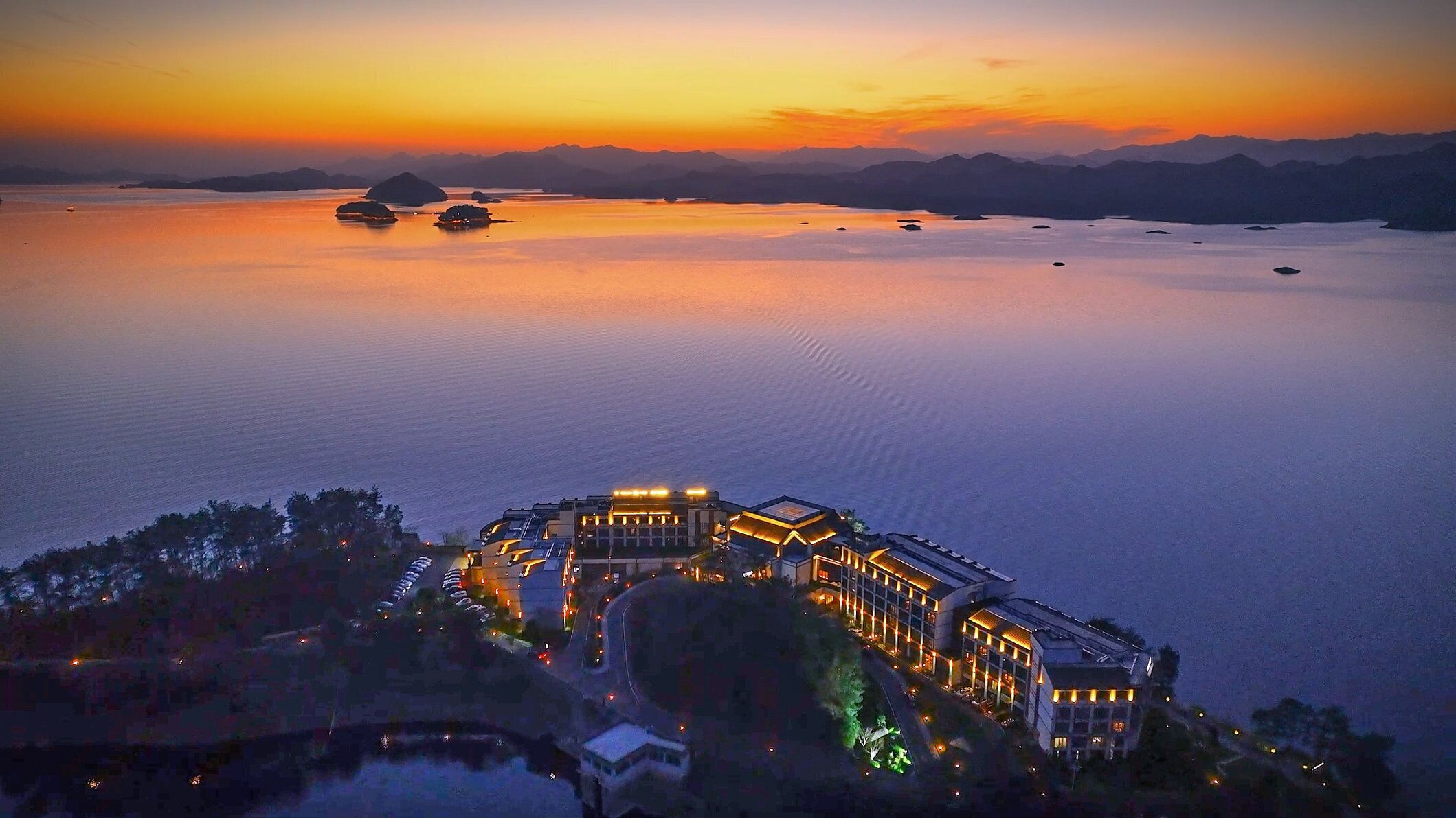 A resort with a large building surrounded by water, multiple boats, and a mountainous backdrop.