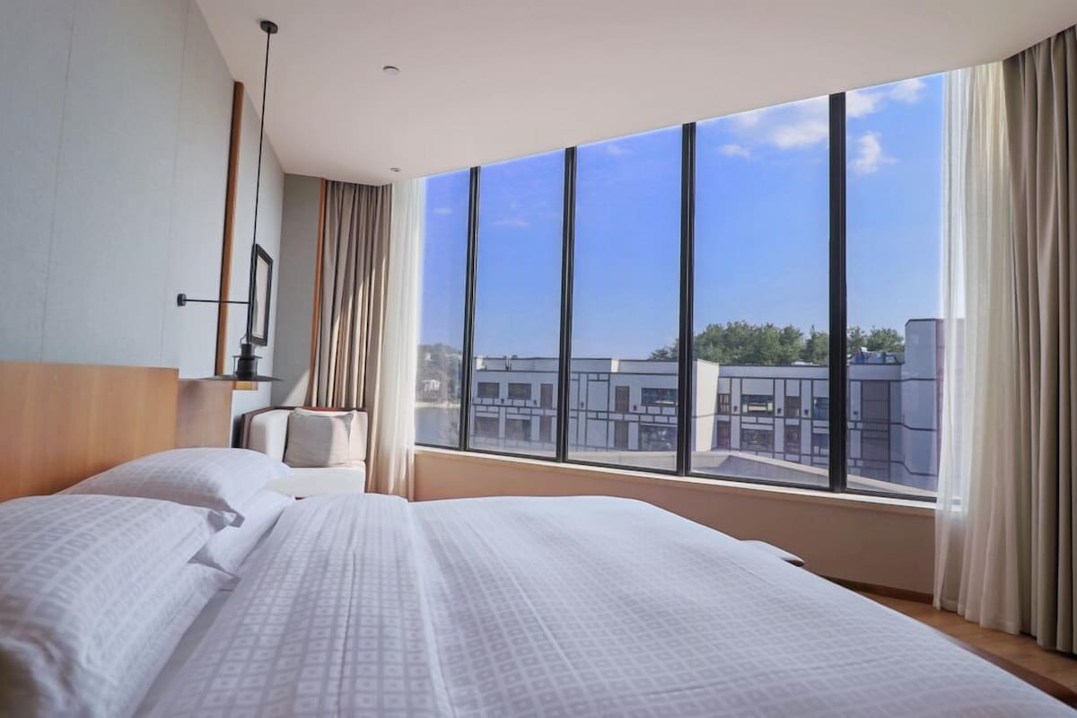 A hotel room with two beds, a large window with a city view, and a modern design.