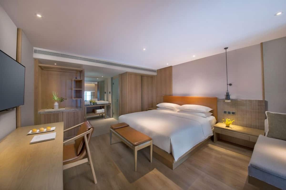 A modern hotel room with a large bed, a desk, a chair, and a TV.
