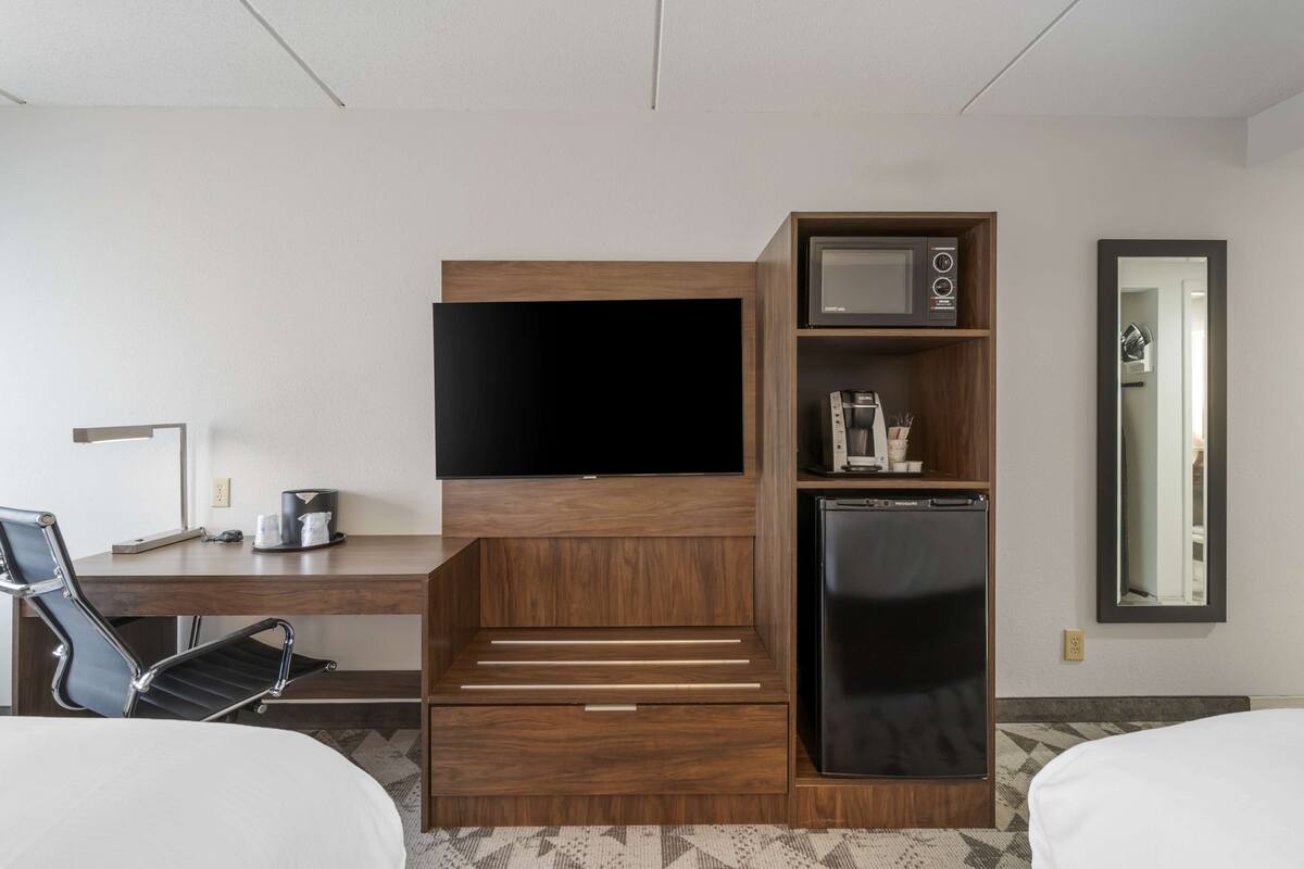 Une chambre d’hôtel équipée d’un bureau en bois, d’un téléviseur à écran plat, d’un four à micro-ondes, d’un réfrigérateur, d’une chaise et d’un lit.