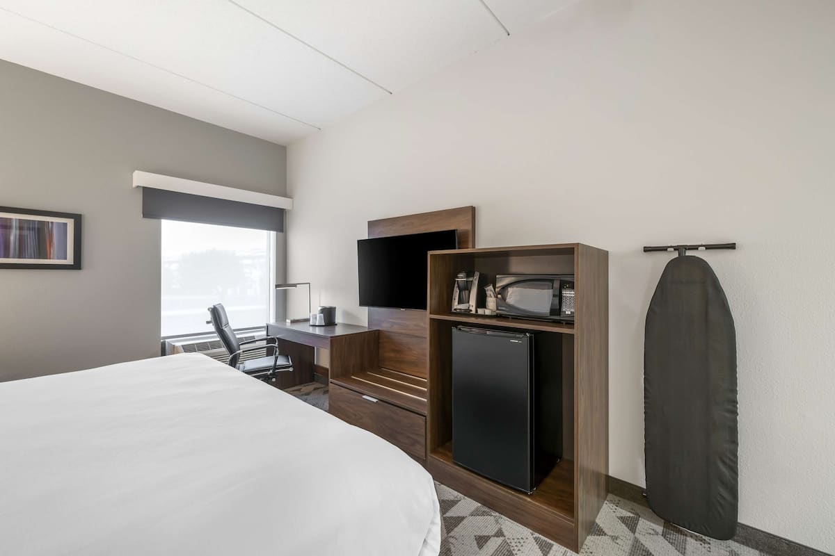 Une chambre d’hôtel équipée d’un lit, d’un bureau avec un ordinateur, d’une télévision, d’un four à micro-ondes et d’un réfrigérateur.