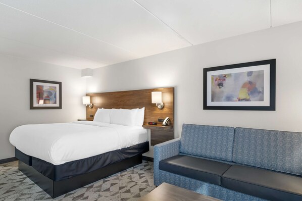 A hotel room with a large bed, a blue sofa, a wooden headboard, two wall-mounted lamps, and two framed artworks.
