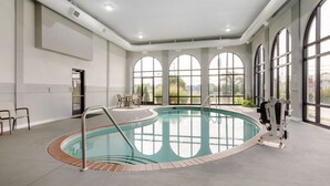 A large indoor swimming pool with a clear view of the outdoors through arched windows, a pool ladder, and a few chairs near the pool. - Best Western Plus Harrisonburg (Harrisonburg)